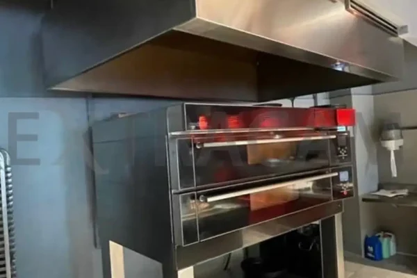 Campana de acero inoxidable instalada sobre un horno de pisos en una cocina industrial